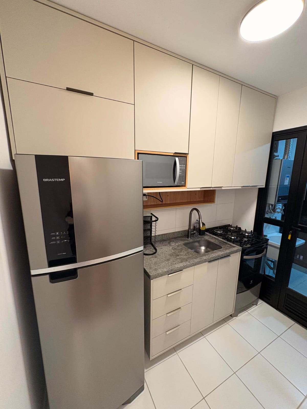 Cozinha compacta com armários em tom bege e geladeira inox